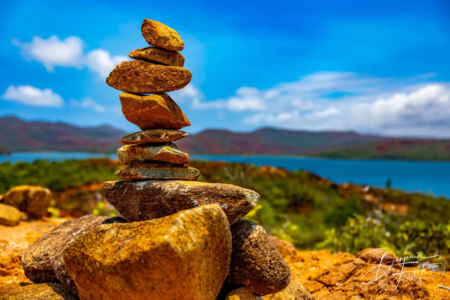 A cairn of stacked stones facing the lagoon, on red earth