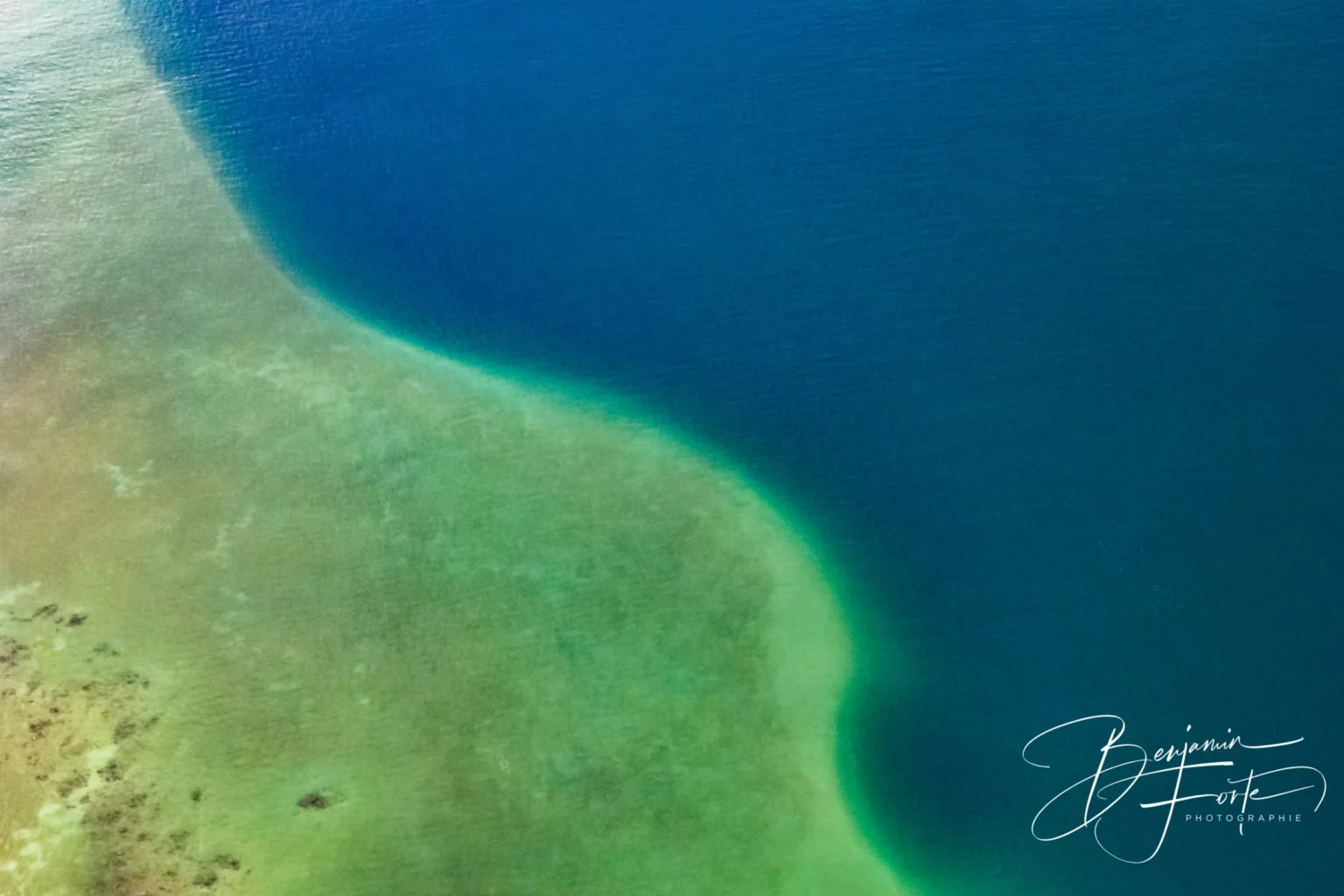 Aerial view of the line between a turquoise shallow and the deep water of the lagoon