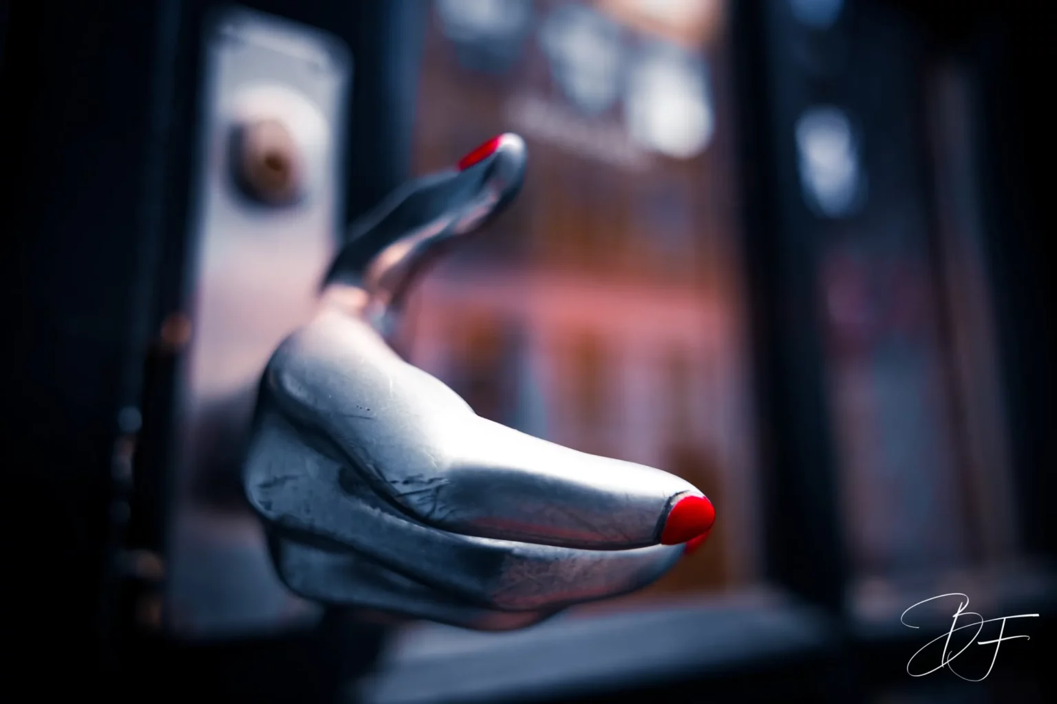 A sculpted hand in silver metal, with red nails, reaching forward