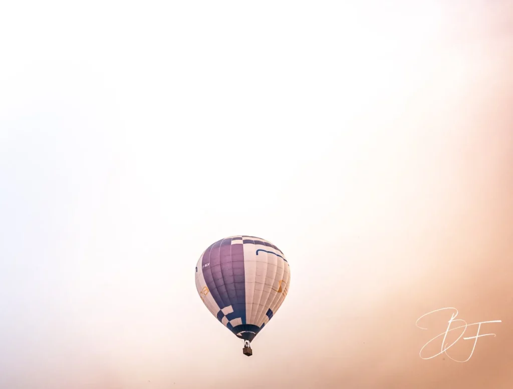 A hot-air balloon rises into a pink sky