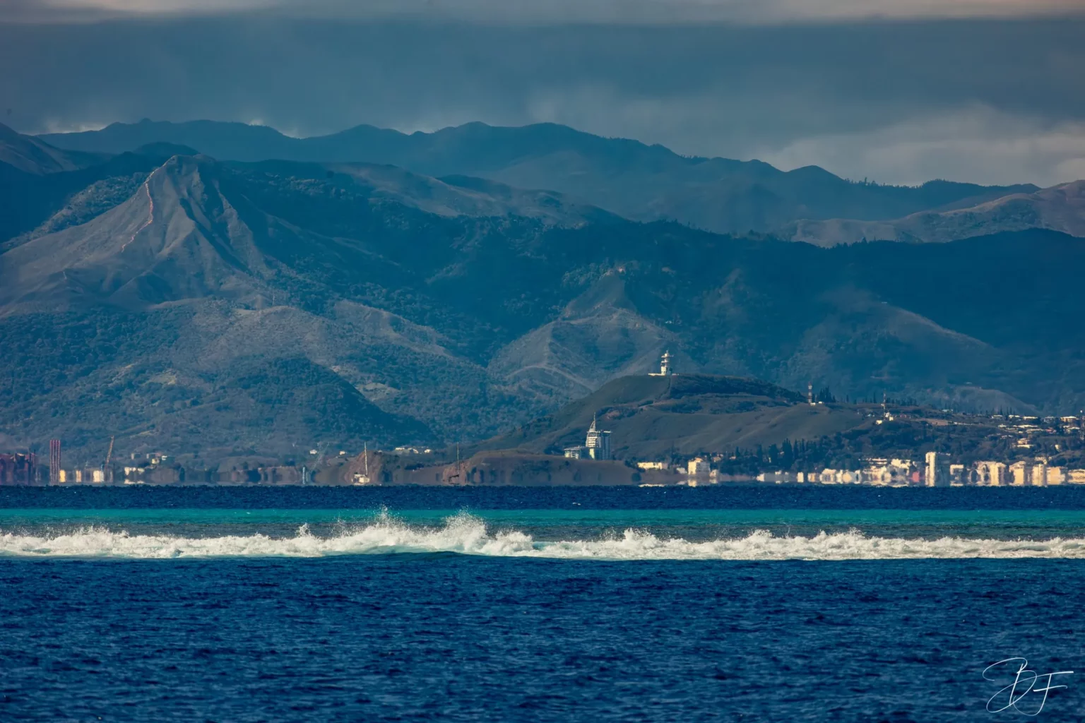 The Nouméa coastline and its mountains seen from the lagoon, a wave breaking on the reef