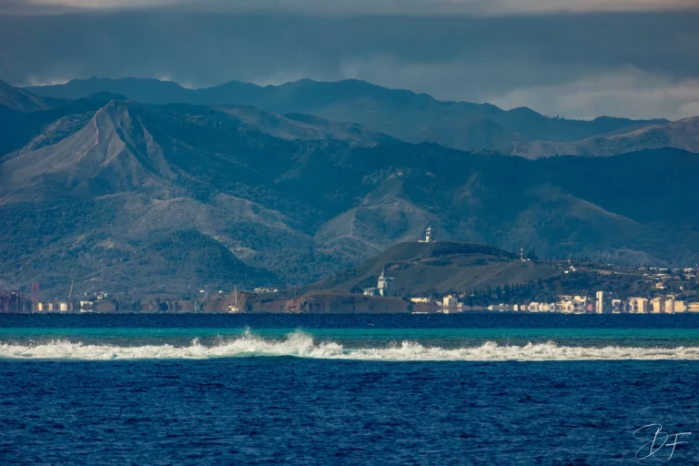 La côte de Nouméa et ses montagnes vues depuis le lagon, une vague déferlant sur le récif