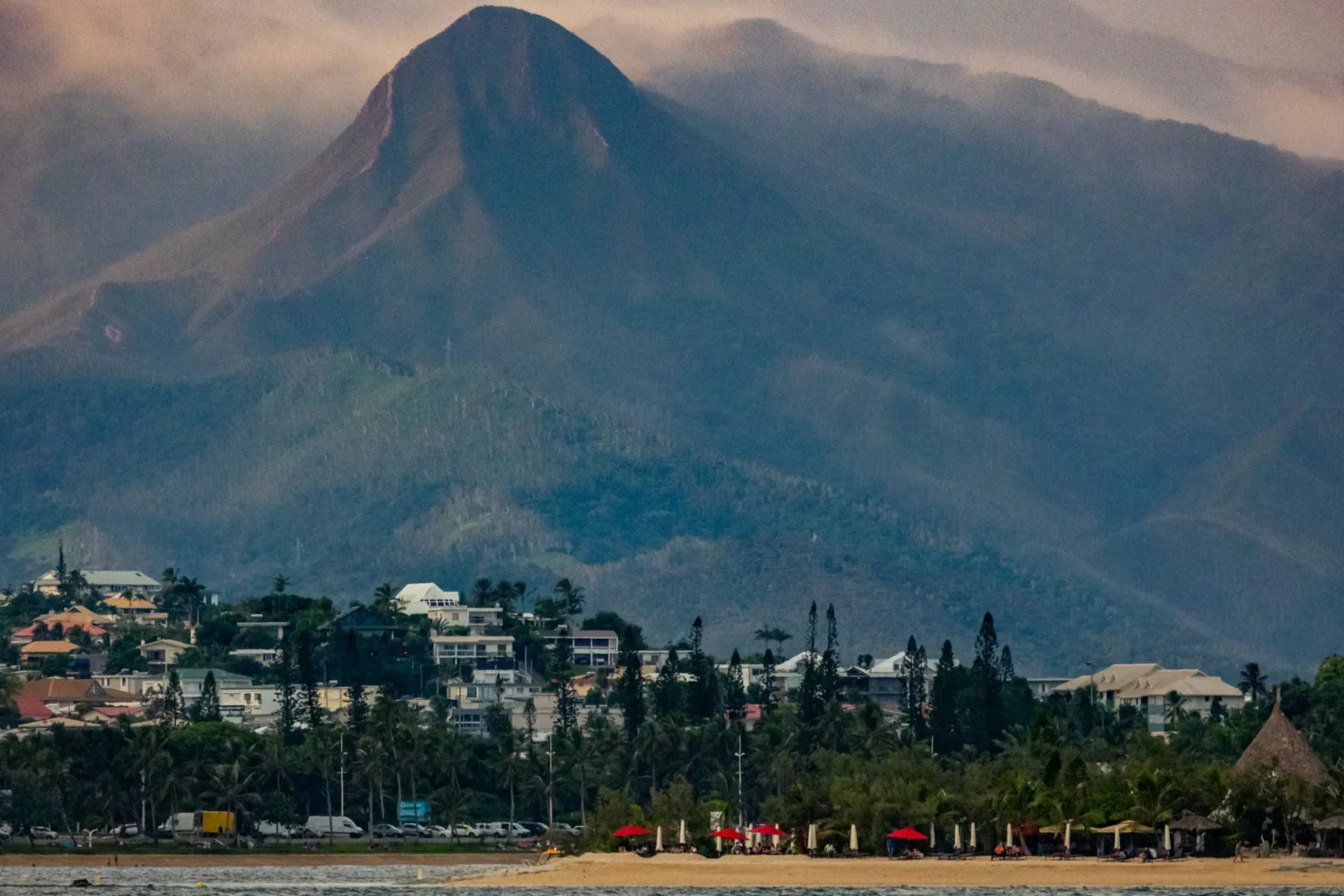 A peak towering over a beach lined with columnar pines, in New Caledonia