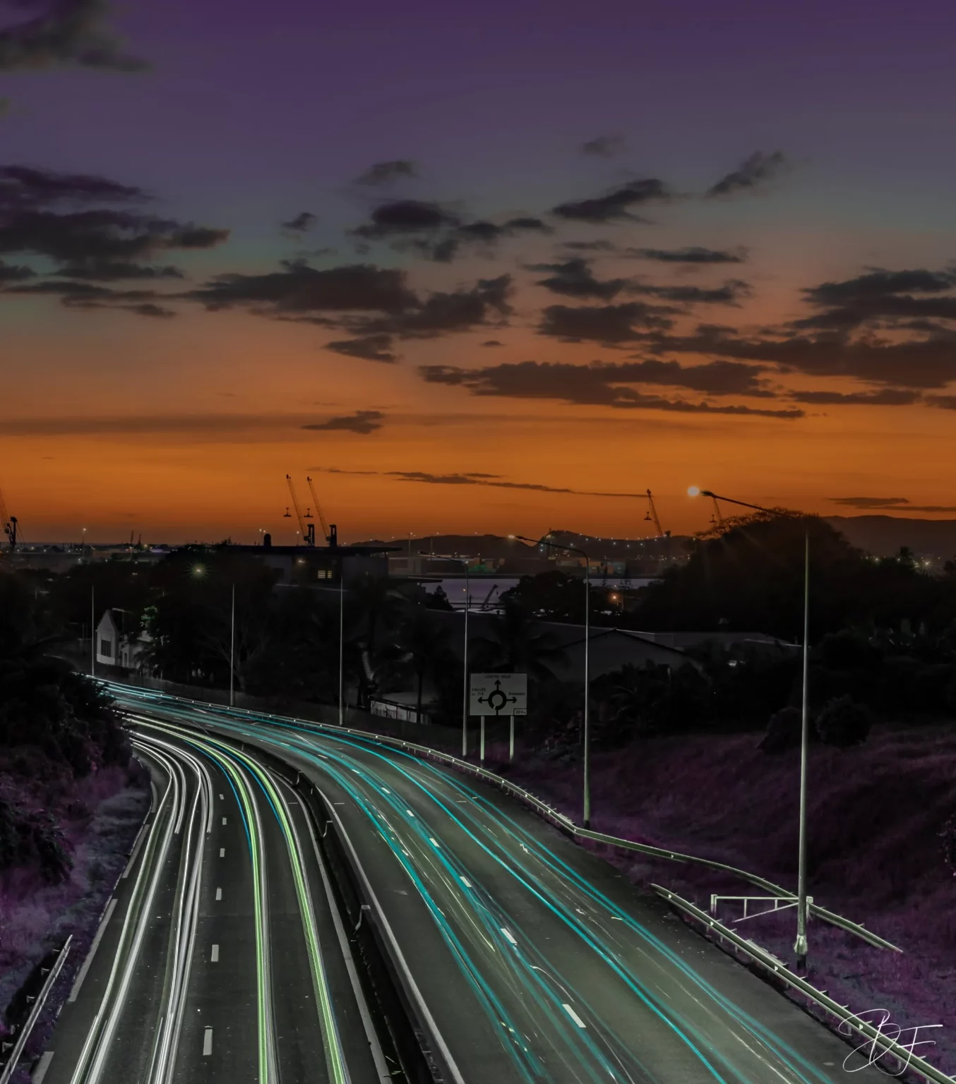 Headlight trails on an expressway at dusk, under an orange sky