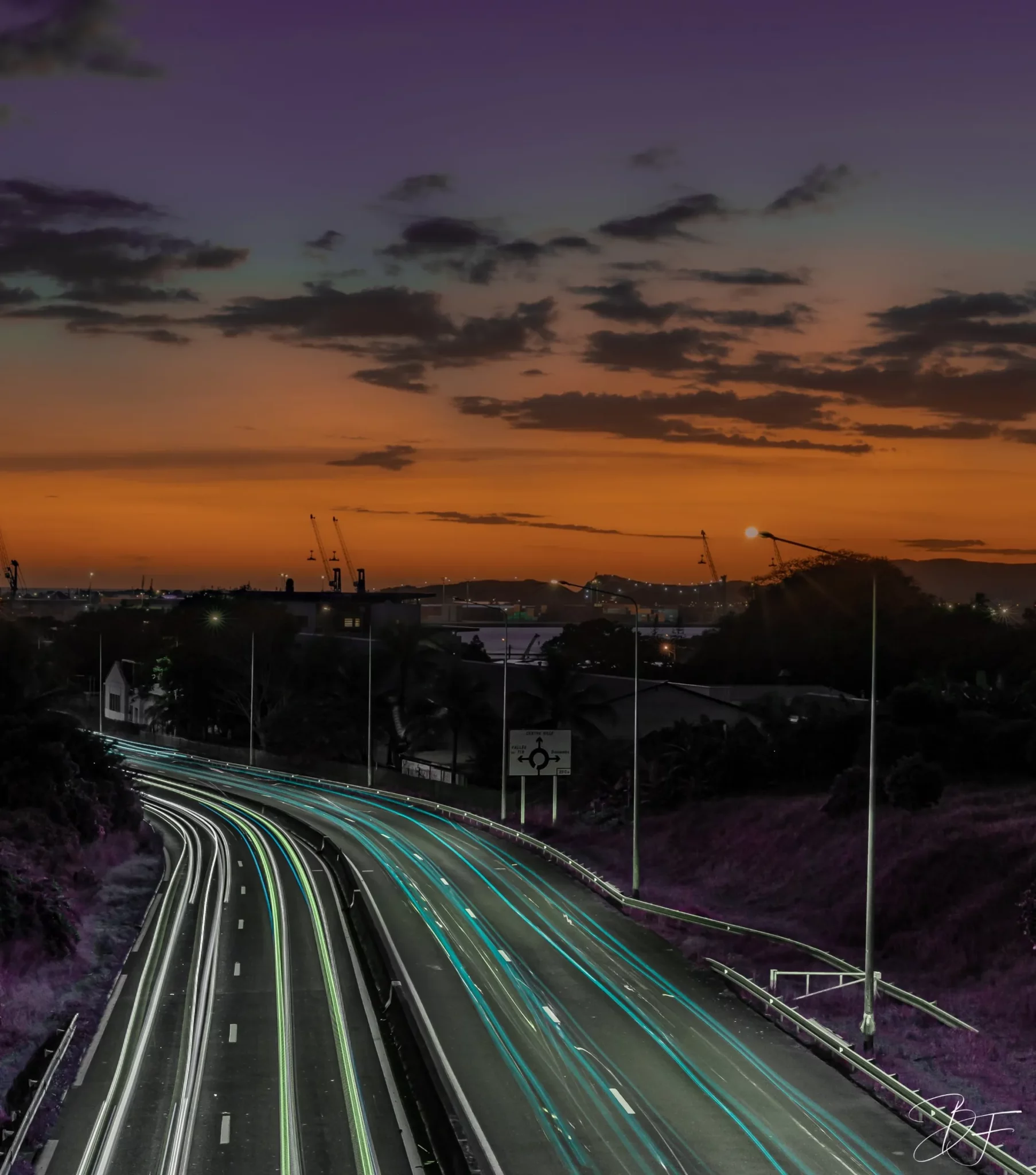 Headlight trails on an expressway at dusk, under an orange sky